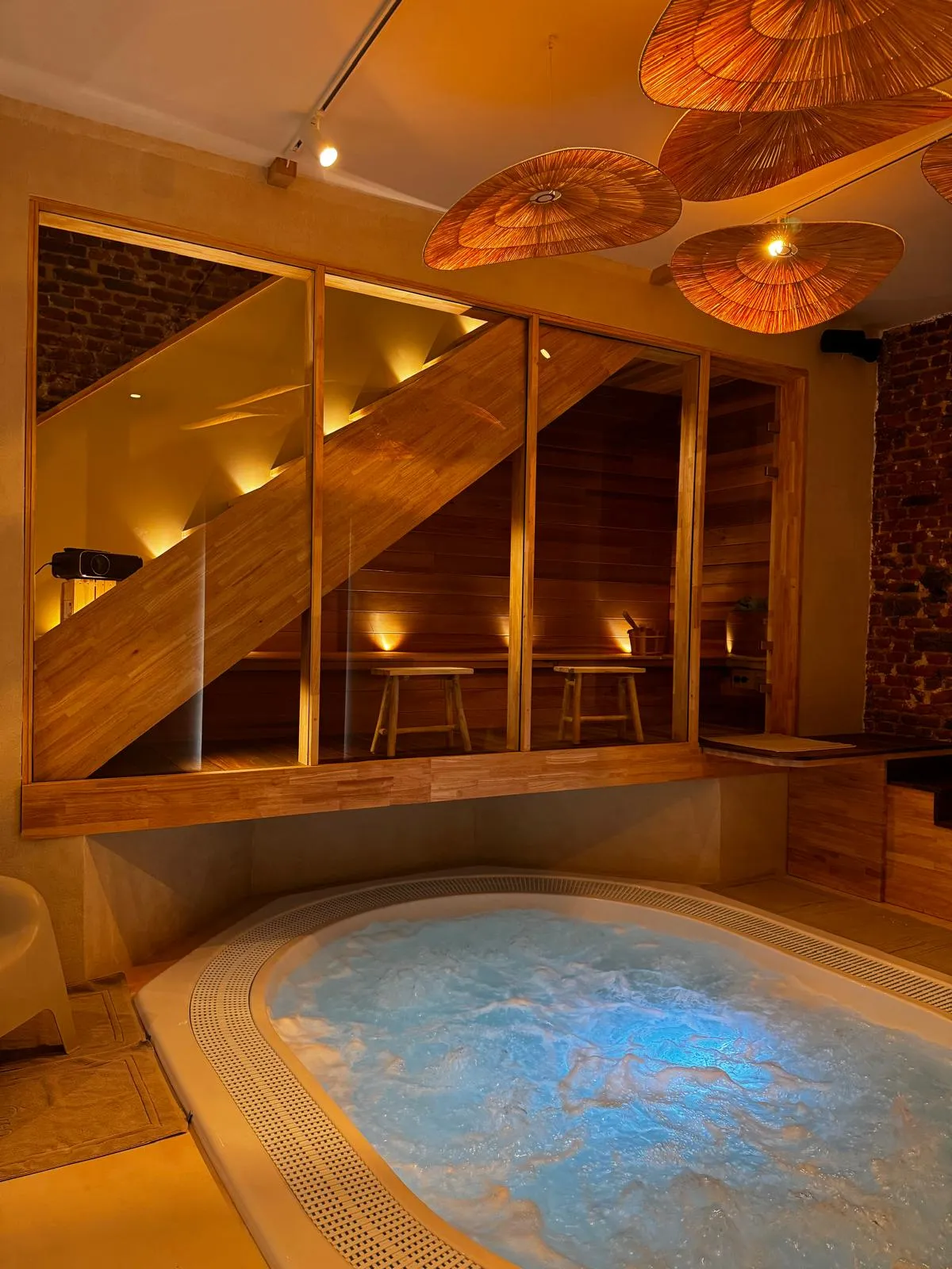 Espace bien-être réalisé par Cube Concept : jacuzzi encastré et sauna vitré sous l'escalier